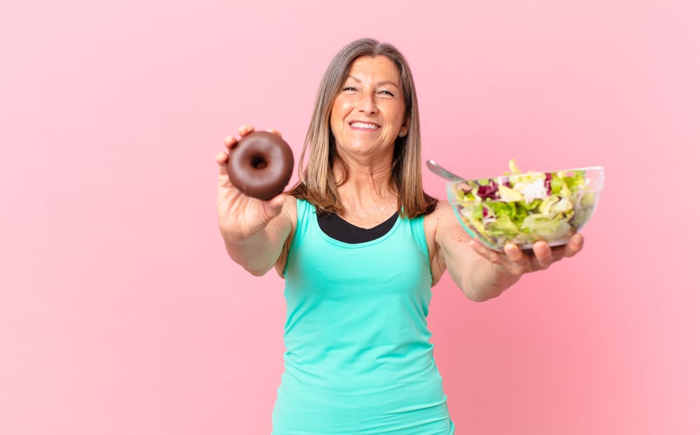 middle age pretty woman coparing a salad and donut